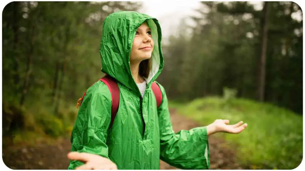 a person in a green raincoat standing in the woods