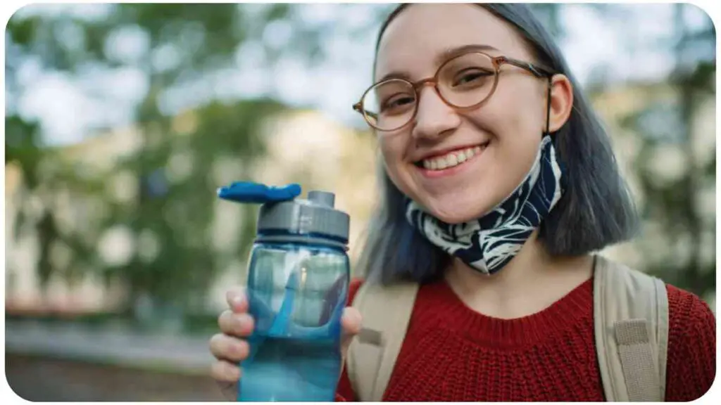 a person with glasses and a scarf is holding a water bottle.